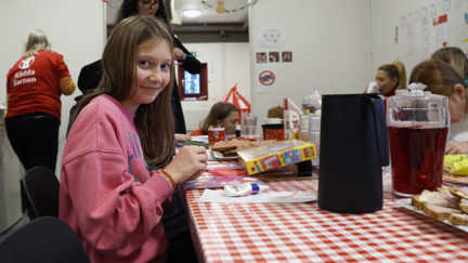 Bild på en flicka i mellanstadieåldern på en barnvänlig plats i Halmstad. Hon sitter vid ett bord och pysslar samtidigt som hon ler mor kameran.