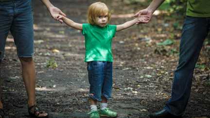 Ett litet barn håller sina föräldrar i händerna.