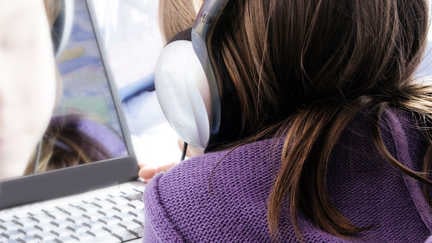 En flicka med hörlurar använder en laptop.