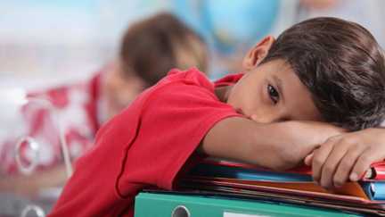 En pojke som lutar sig mot en hög pärmar.