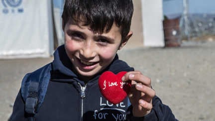 En liten pojke som håller i ett rött hjärta med texten "I love You"