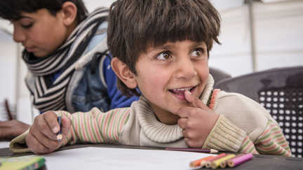 Ibrahim, 7 år, sitter vid ett bord och ritar på Rädda Barnens barnvänliga plats i ett flyktingläger i Syrien