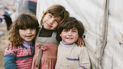 re flickor utanför ett tält i ett flyktingläger i Irak
